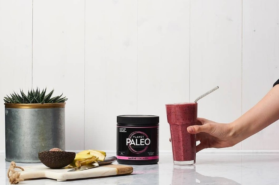Planet Paleo Marine Collagen tub beside a berry smoothie with metal straw; hand lifting the glass; avocado and ginger on a board.